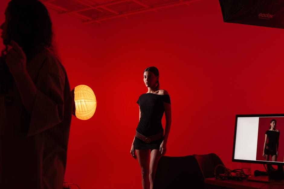 Elegant fashion model posing in bold red-lit studio for creative photoshoot.